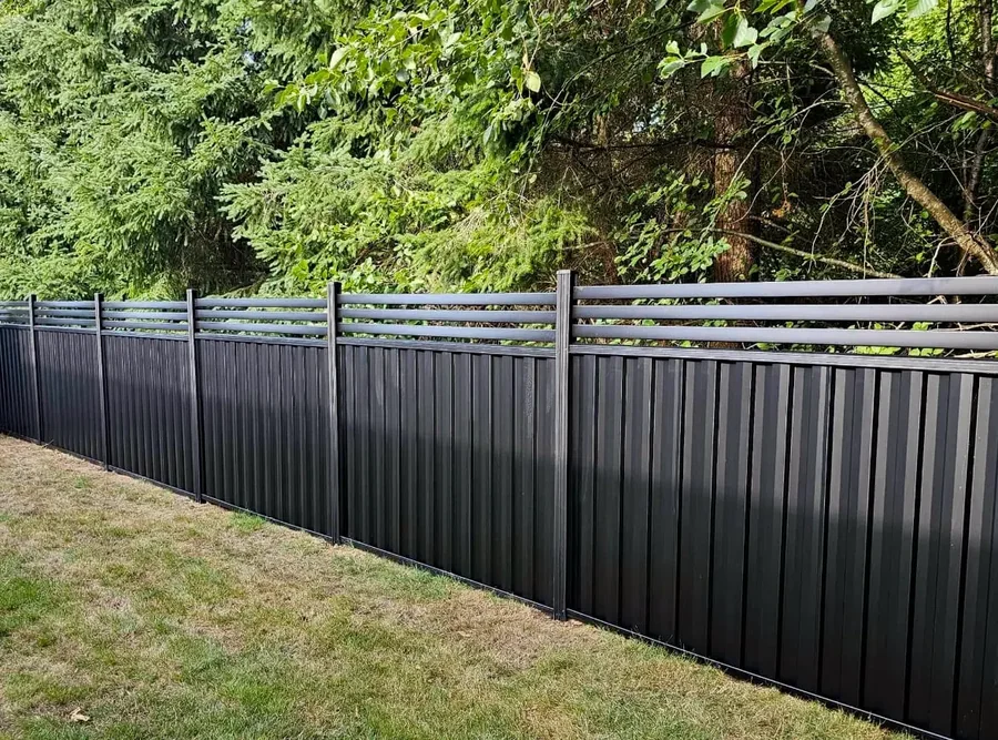 Black aluminum privacy fence installed along a lawn at the treeline.